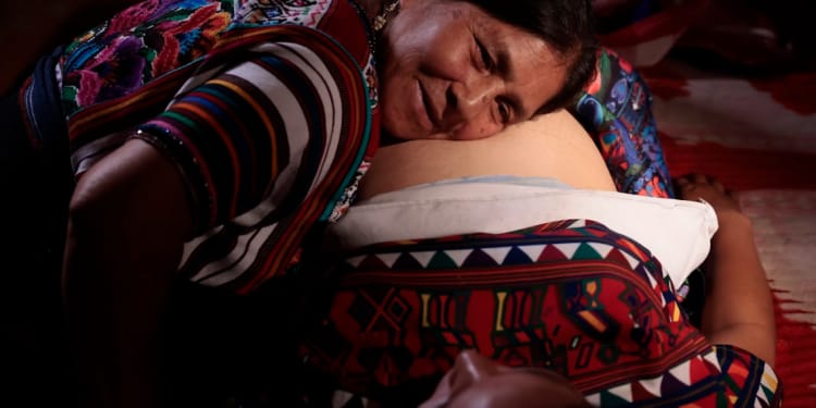 A traditional midwife listening with her ear against a pregnant woman’s abdomen.
